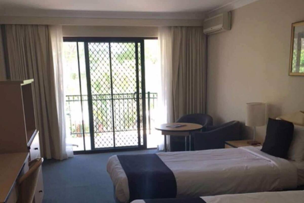 Camera d'albergo con due letti, una scrivania, una sedia, un tavolino e un balcone con vista.