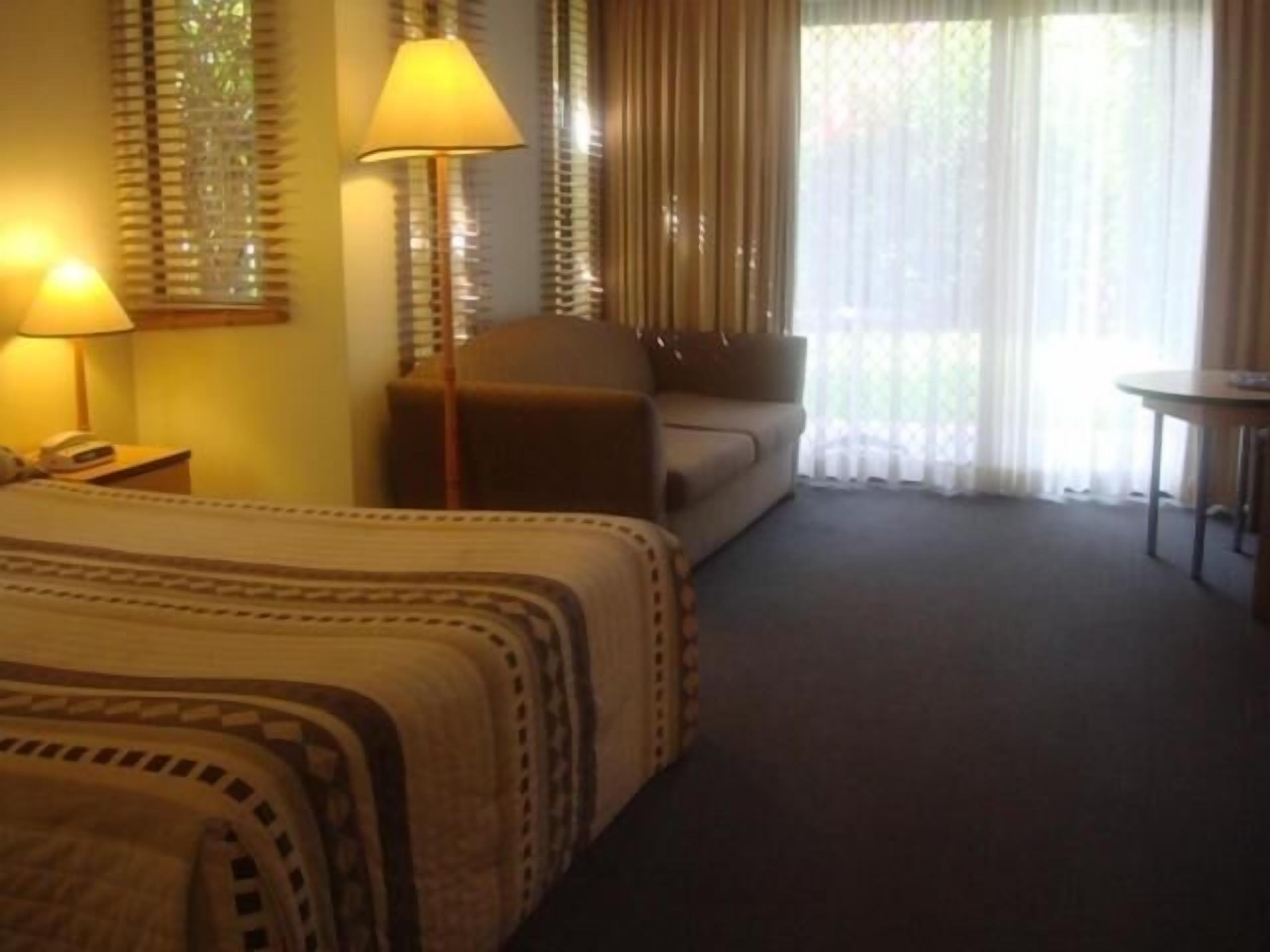 A hotel room with a bed, a sofa, a table, and a lamp.