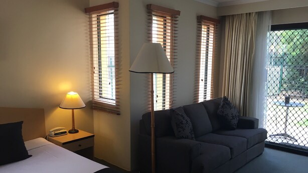 Una habitación de hotel con cama, sofá, lámpara y ventanas con persianas.