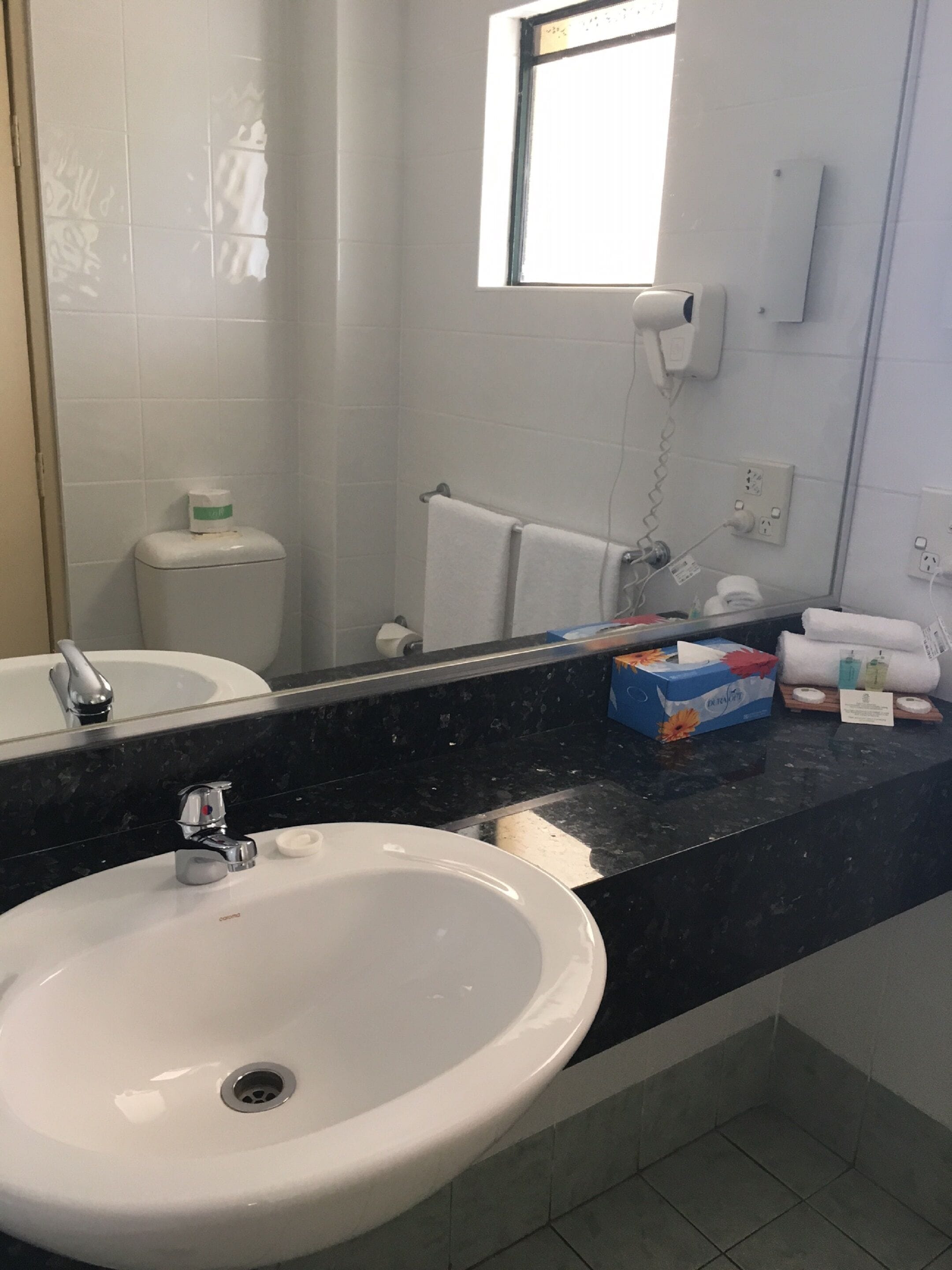 A bathroom with a white sink, a mirror, a towel rack, and a window.