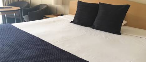 Una habitación de hotel con una cama grande, una mesita de noche, una lámpara, una silla y una pequeña mesa.
