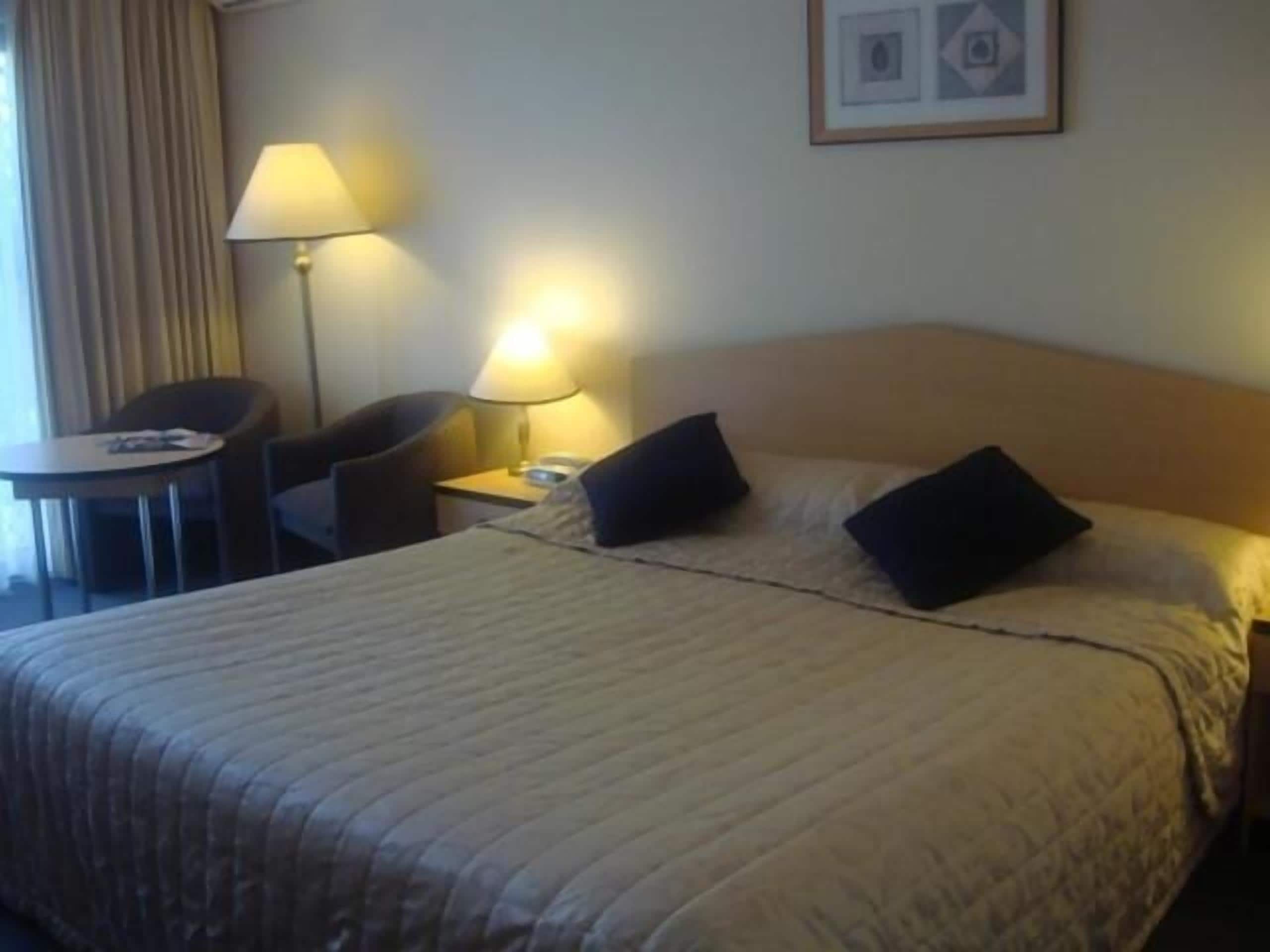 Een hotelkamer met een bed, een bureau, een stoel, een lamp en een lijst met een afbeelding aan de muur.