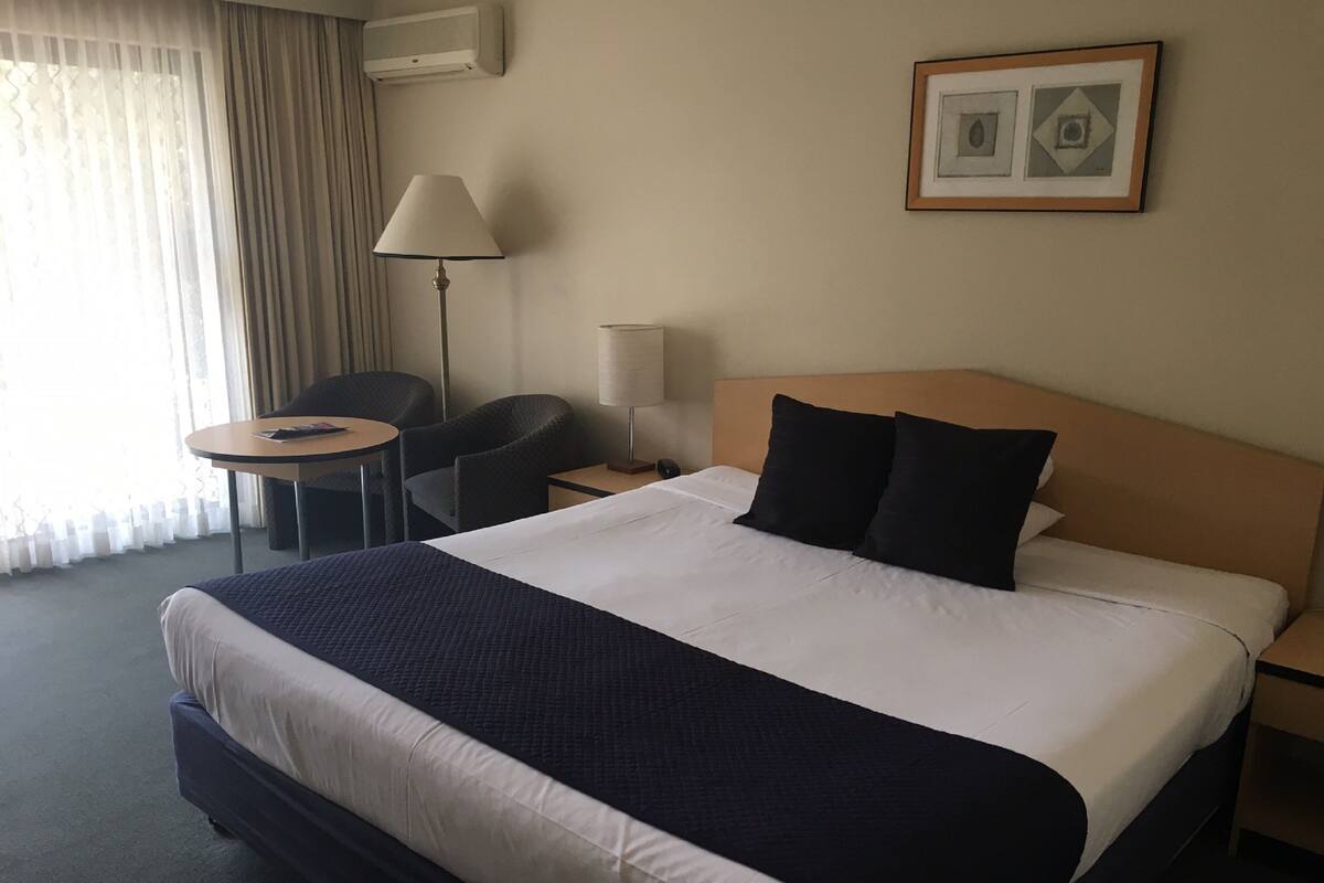Una camera d'albergo con un letto grande, un comodino, una lampada, una sedia e un tavolino.