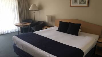 Et hotelværelse med en stor seng, et sengebord, en lampe, en stol og et lille bord.