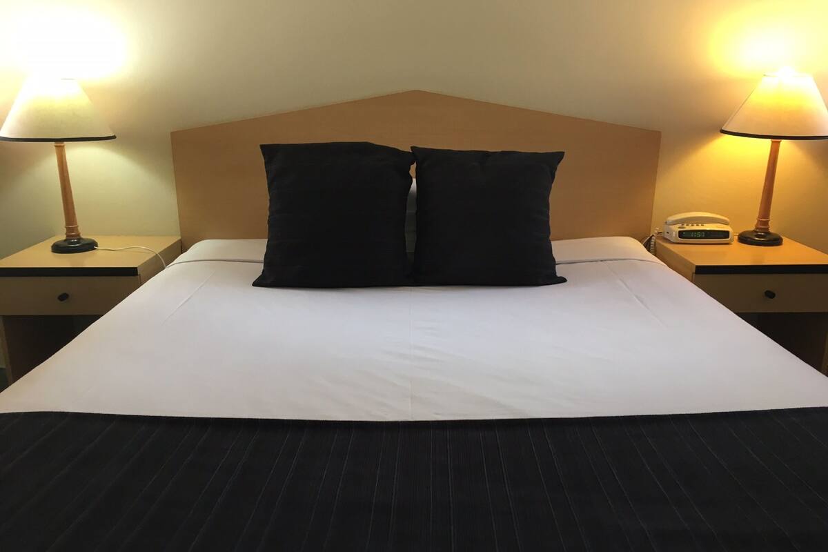 Un letto rifatto con due cuscini neri, un piumone bianco e una coperta nera. Due comodini con lampade, uno per lato del letto.