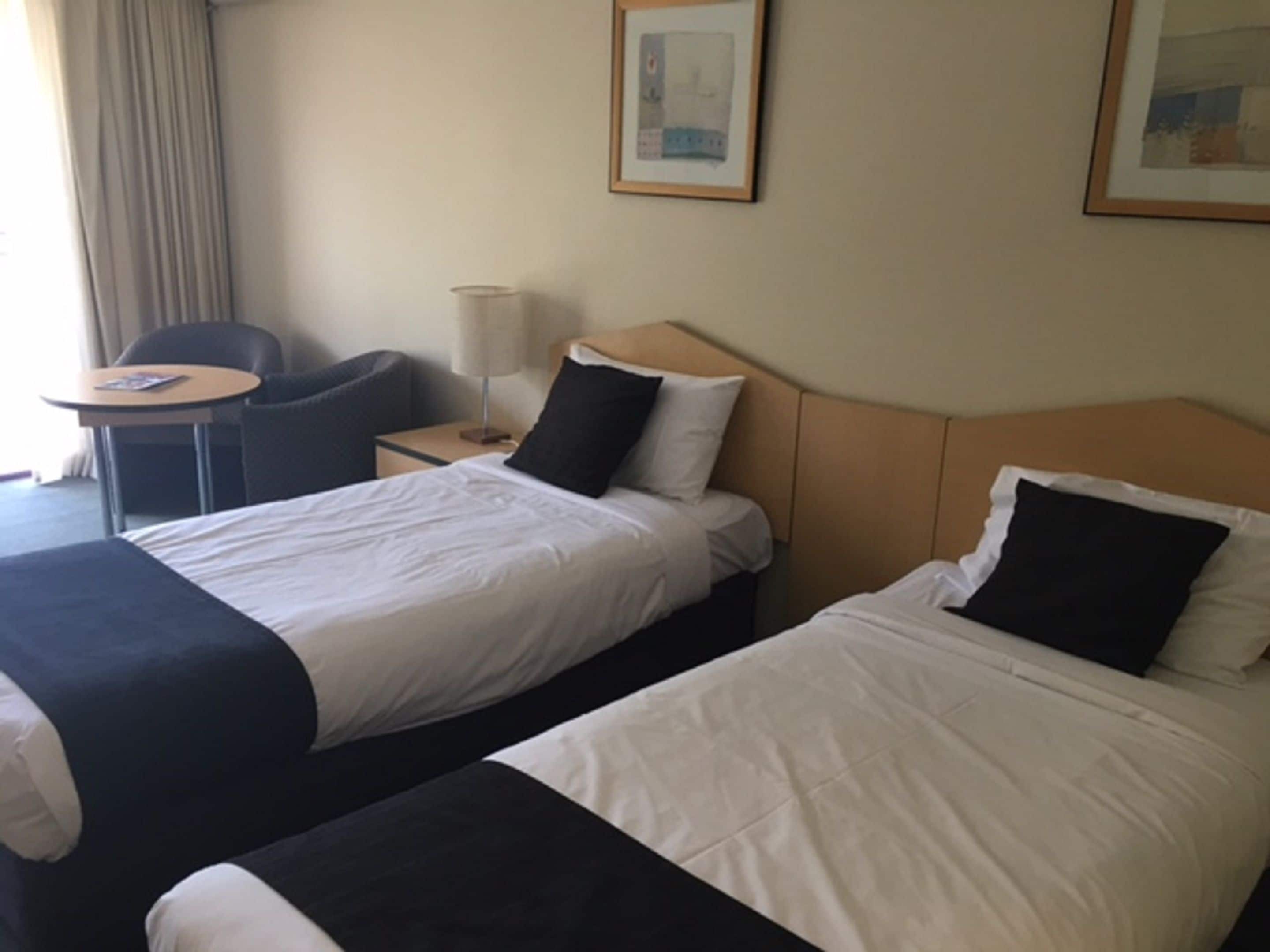 Une chambre d’hôtel avec deux lits, une petite table, une chaise et une lampe.