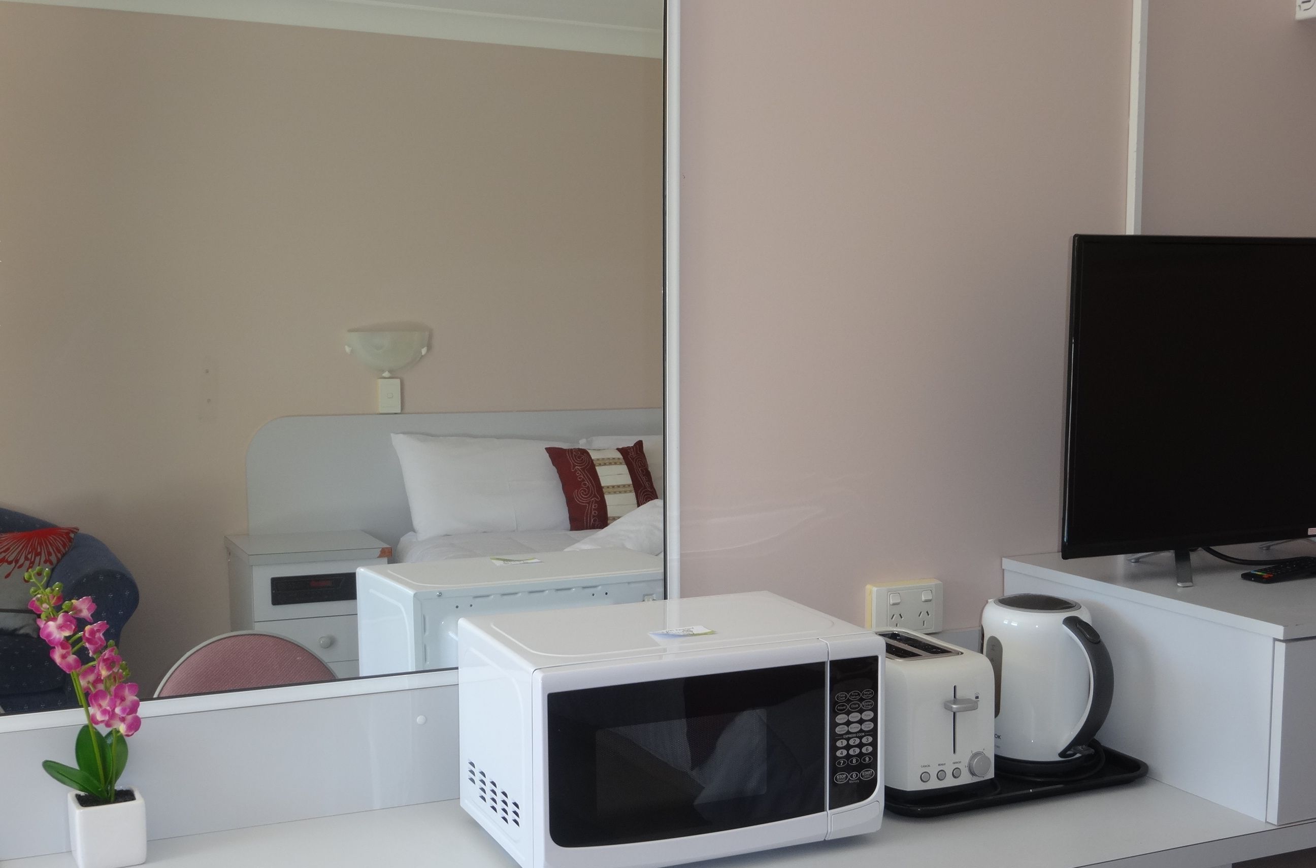 A hotel room with a white microwave, toaster, and coffee maker on a counter, a bed with pillows, and a TV on a stand.