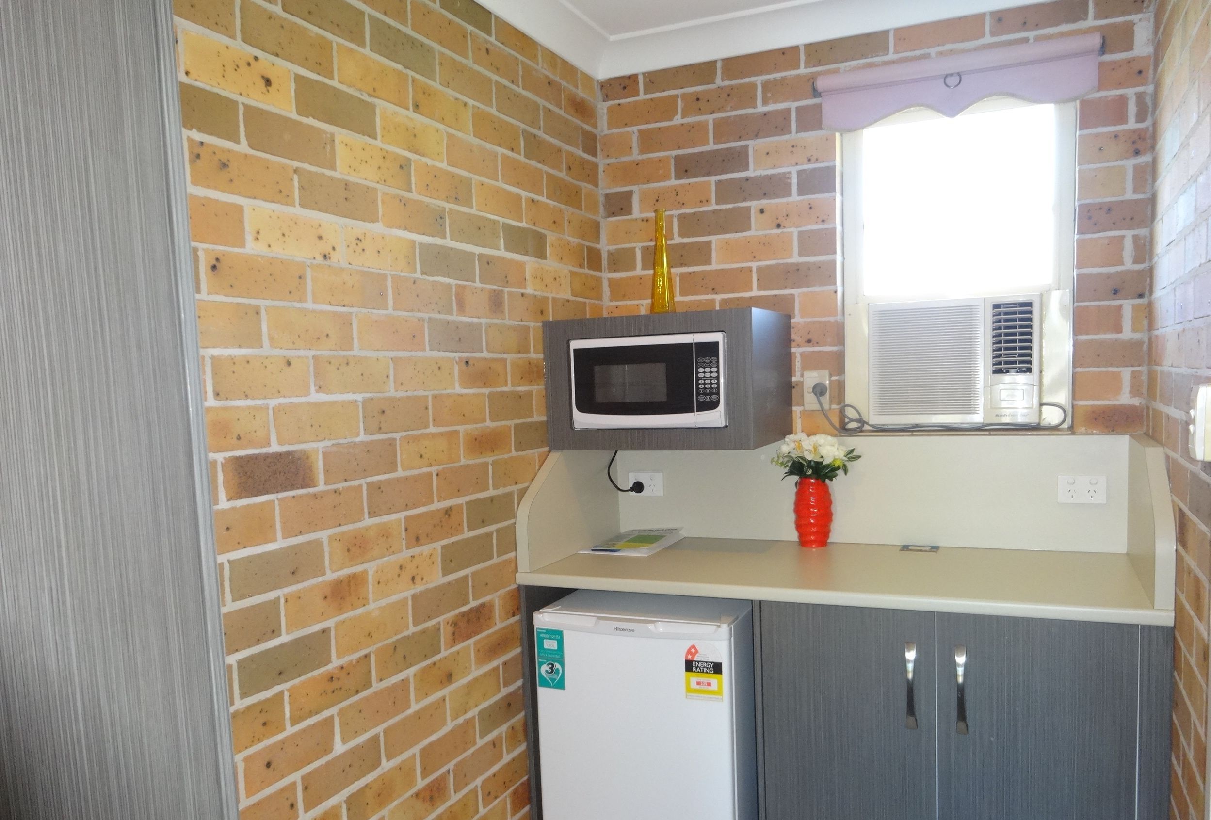 A compact kitchen with a microwave, a small refrigerator, and a window with blinds.