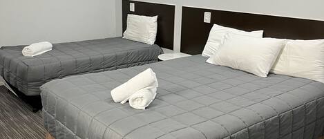 A hotel room with two beds, each with a grey quilted bedspread and white pillows, a ceiling fan, and a painting on the wall.