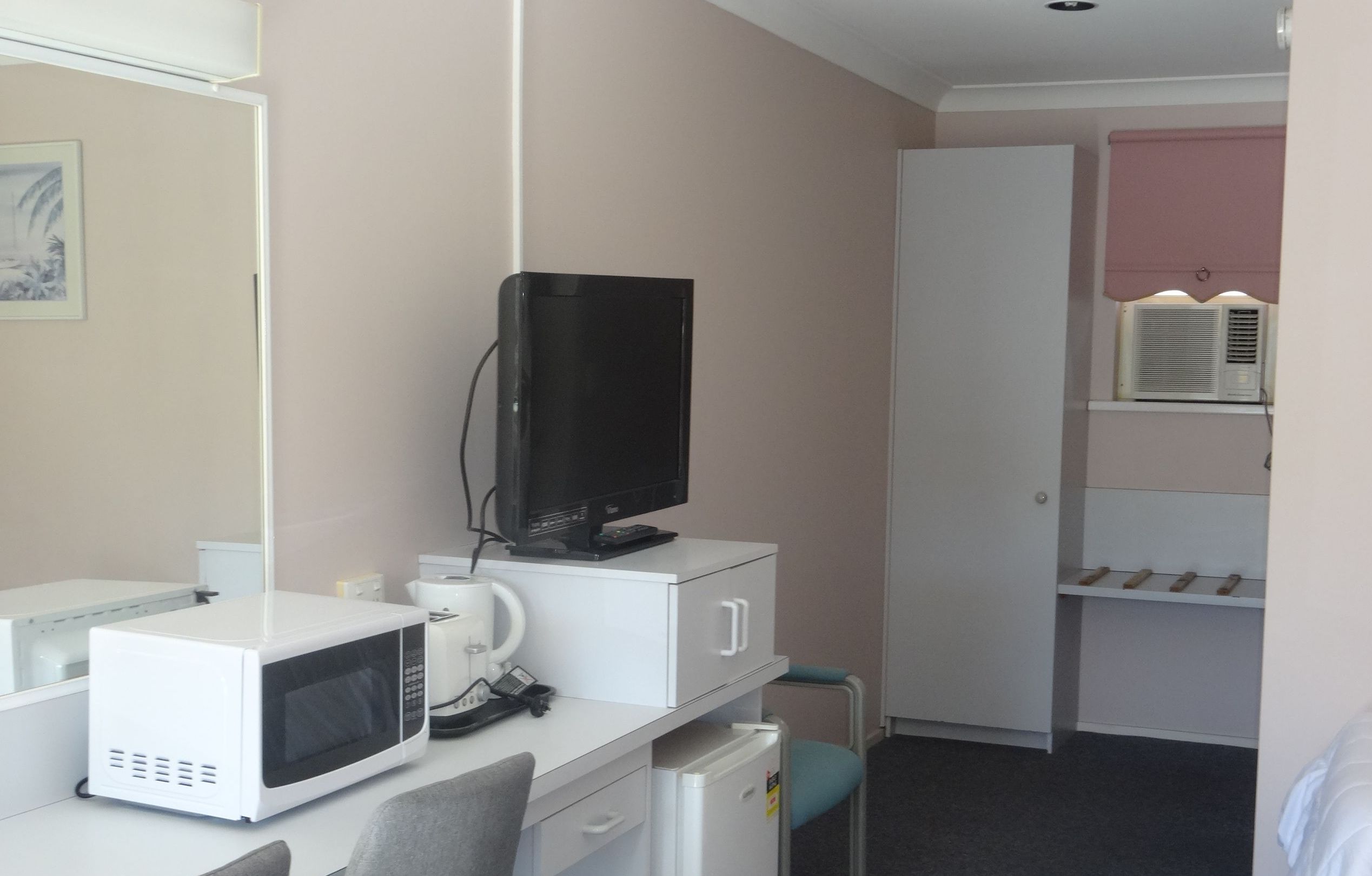 A compact hotel room with a kitchenette, a television, a microwave, a small refrigerator, a desk, and a wardrobe.