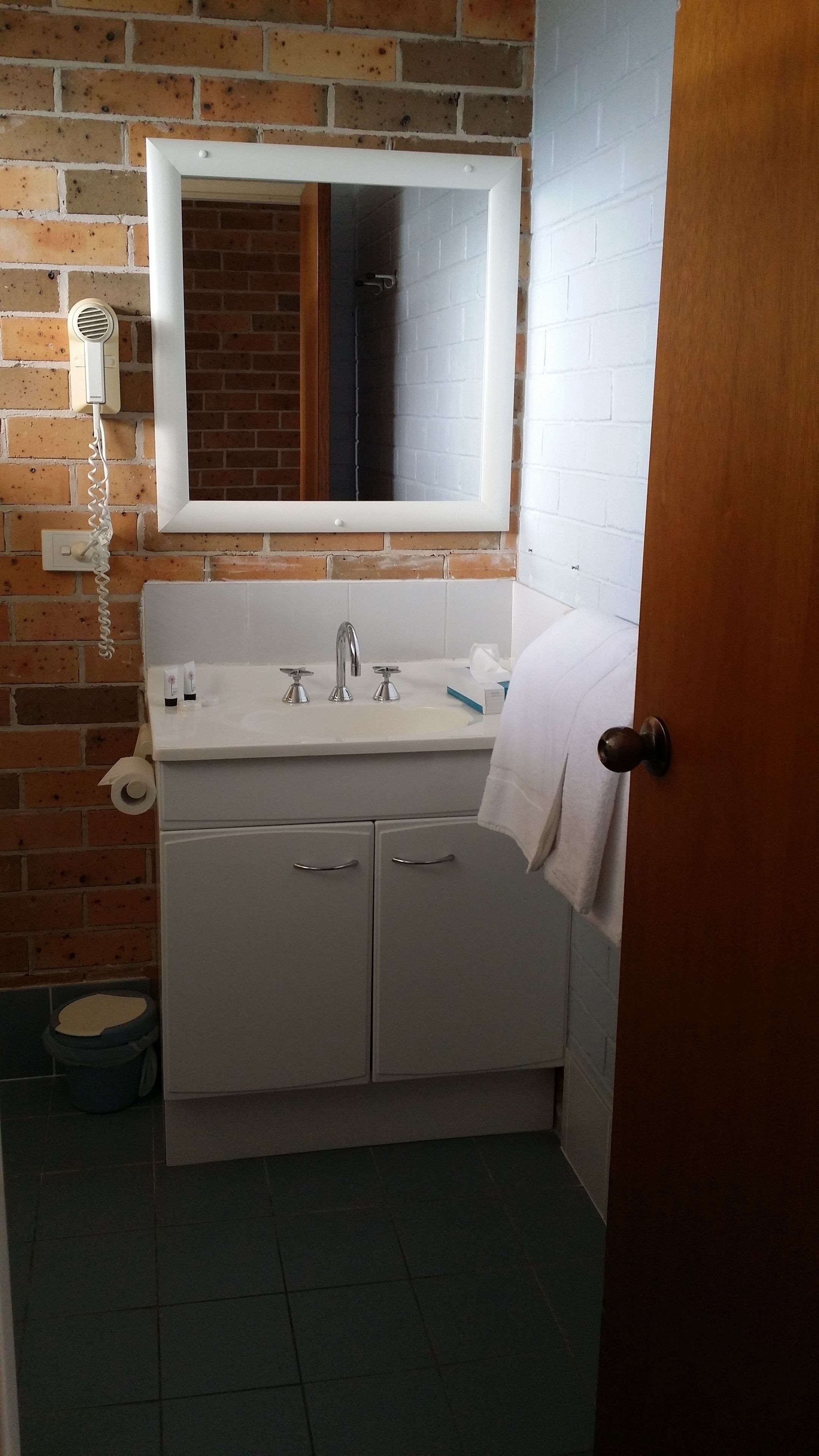 A bathroom with a white sink, two faucets, a mirror above the sink, a hairdryer on the wall, and a toilet.