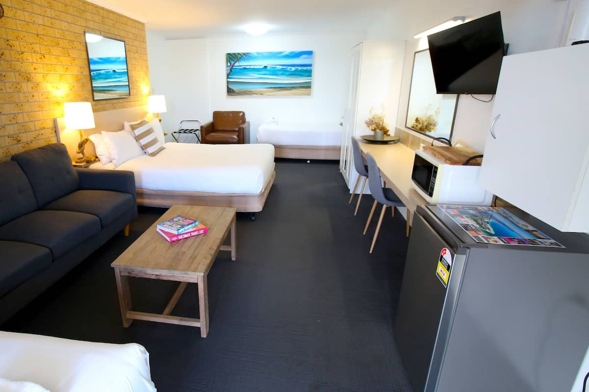 A compact hotel room with a sofa, a bed, a small table with a book, a TV, and a refrigerator.