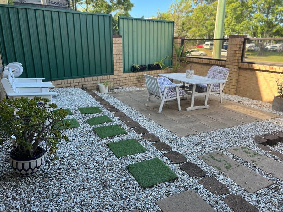 A patio with a white table and chairs, surrounded by a gravel path with green squares.