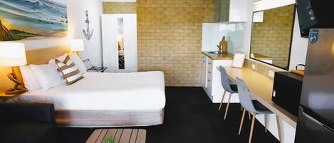 Habitación de hotel con cama, escritorio, sillas, una pequeña planta en maceta, televisión y pared de ladrillo.