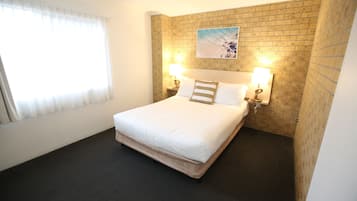 Ein Hotelzimmer mit einem Bett, zwei Nachttischlampen, einem Deckenventilator, einem Fenster mit Vorhängen und einer Wand mit Ziegeloptik.