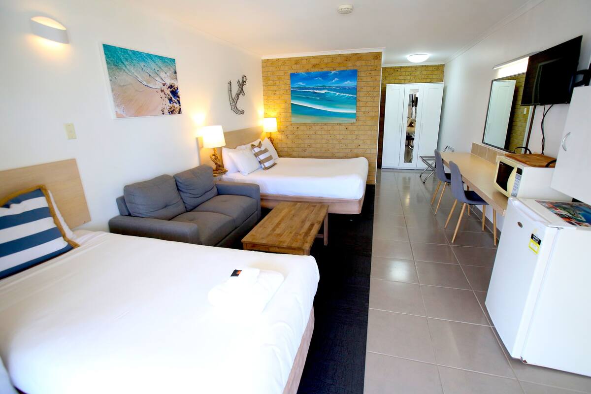 A hotel room with two beds, a sofa, a desk, and a TV.