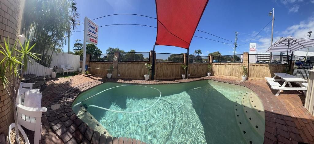 A swimming pool with a red shade sail, a white fence, and a sign indicating a motor home rental service.