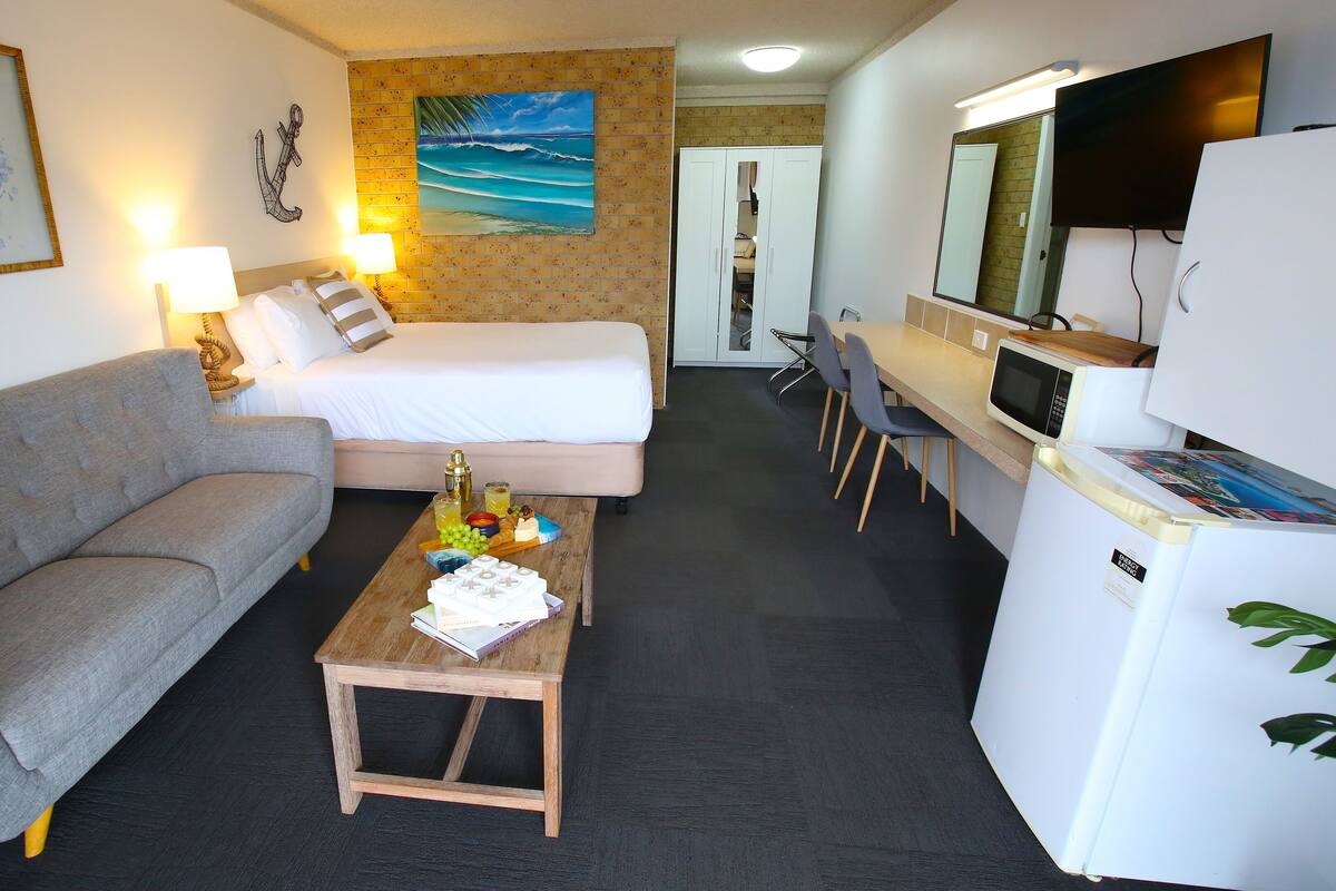A hotel room with a sofa, a bed, a desk with a computer, and a TV.