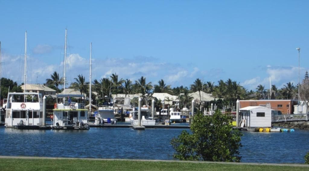 A marina with boats docked, a small building, and palm trees in the background.