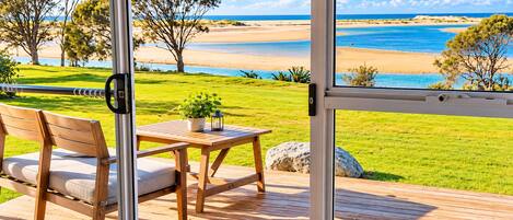 Una terraza con una mesa y silla de madera, con vista a una playa y cielos despejados.
