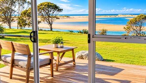 A deck with a wooden table and chair, overlooking a beach with clear skies.