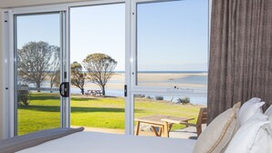 A bedroom with a large window overlooking a beach and grassy area.