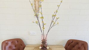 Une table à manger avec deux chaises en cuir marron, un set de table en fibres tressées et un vase orné de branches et de fleurs jaunes.