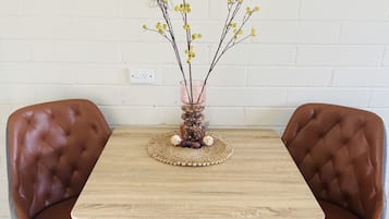 A dining table with two brown leather chairs, a woven placemat, and a vase with branches and yellow flowers.