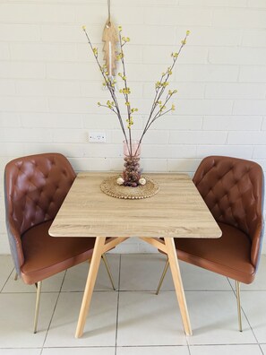 A dining table with two brown leather chairs, a woven placemat, and a vase with branches and yellow flowers. - Pelican Sands Scamander (Scamander)
