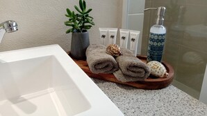 A bathroom with a white sink, a wooden tray with towels, a potted plant, and toiletries.