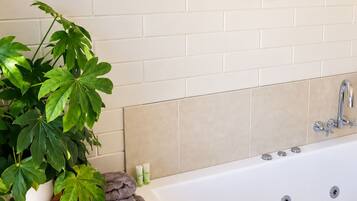 Une salle de bain avec une baignoire blanche, une plante en pot, une serviette et un miroir décoratif accroché au mur.