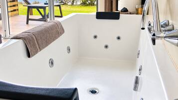 A modern bathroom with a large bathtub, a shower, and a view of the beach.