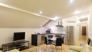 A modern apartment with a living room, a glass coffee table, a TV, a kitchen with a dining area, and a small balcony.