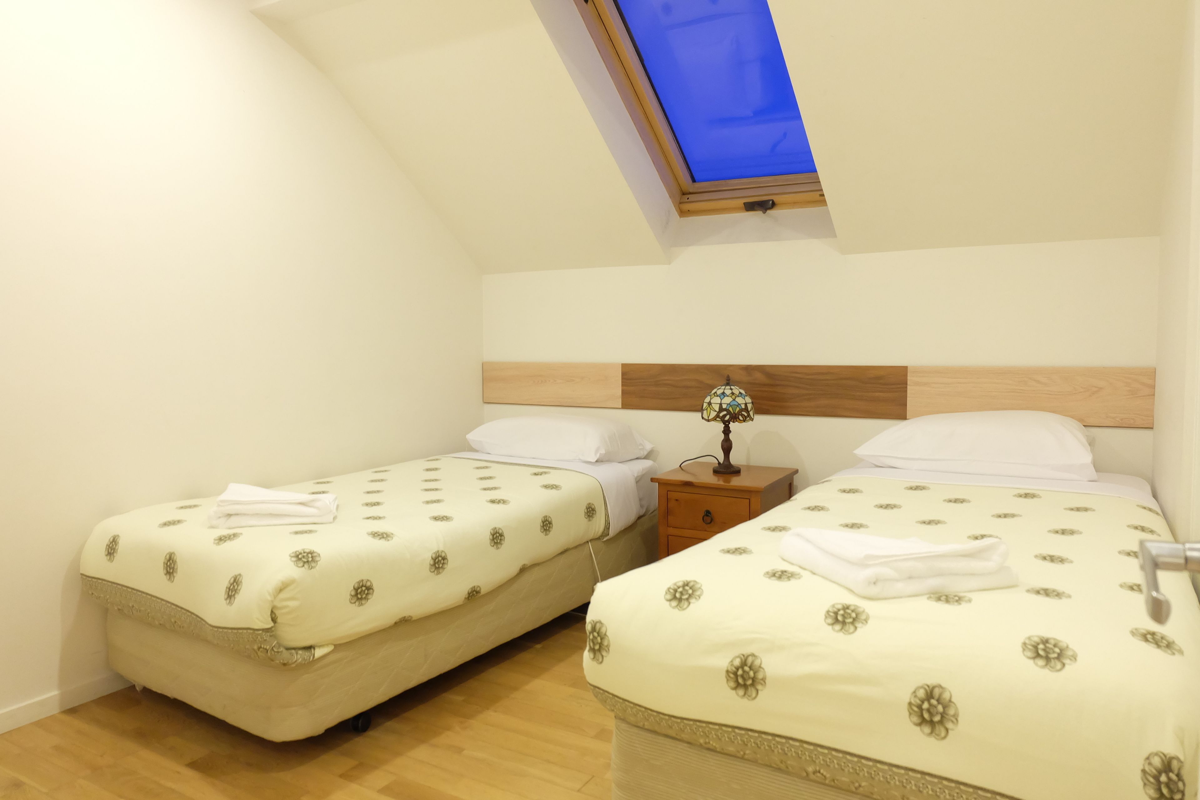 A room with two beds, a wooden headboard, a nightstand, and a skylight.