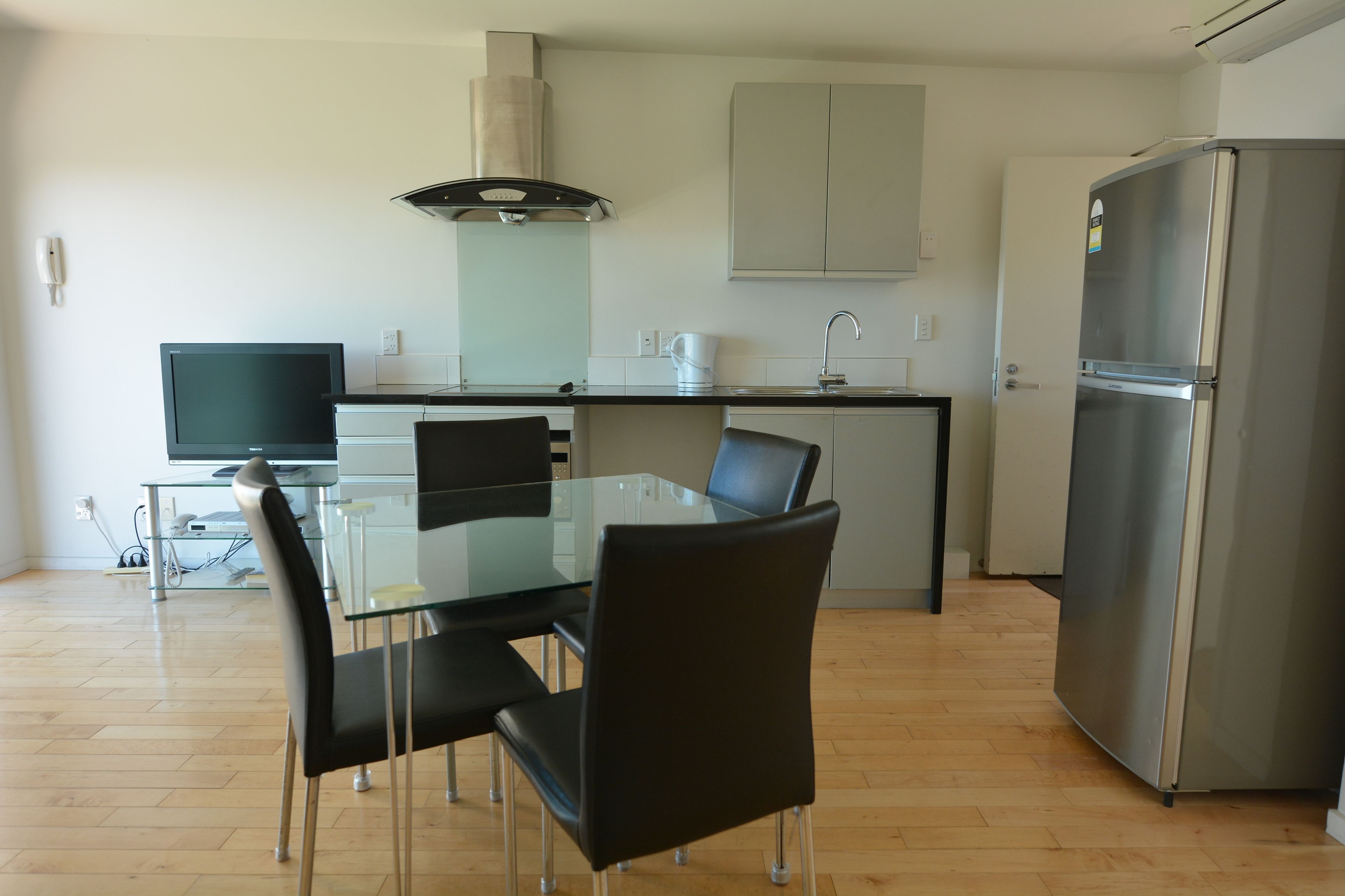 Een moderne keuken met een glazen eettafel, zwarte stoelen, een roestvrijstalen koelkast en een inbouwoven.