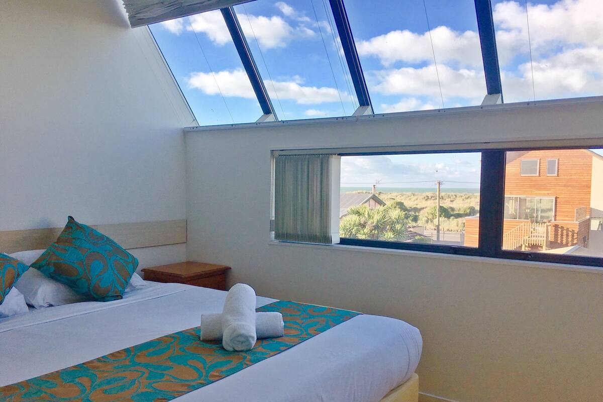 A bedroom with a large bed, a window with a view of the beach, and a skylight.