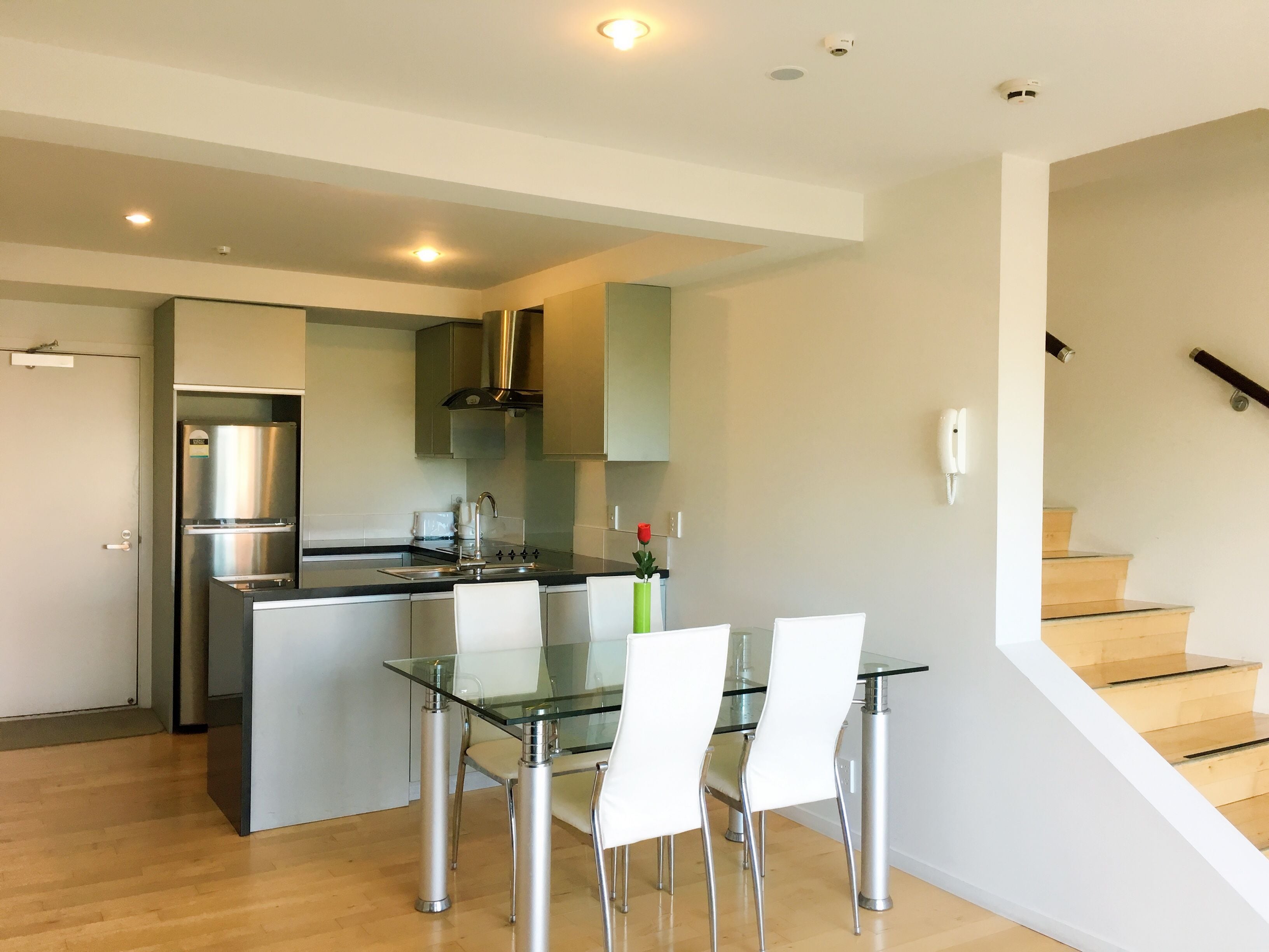 A modern kitchen with stainless steel appliances, a glass dining table, and a staircase leading to an upper level.
