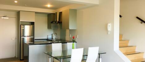 A modern kitchen with stainless steel appliances, a glass dining table, and a staircase leading to an upper level.