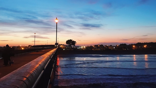 A waterfront promenade with a metal railing, street lamps, and a calm sea reflecting the lights. - Beachlife Apartments (Christchurch)