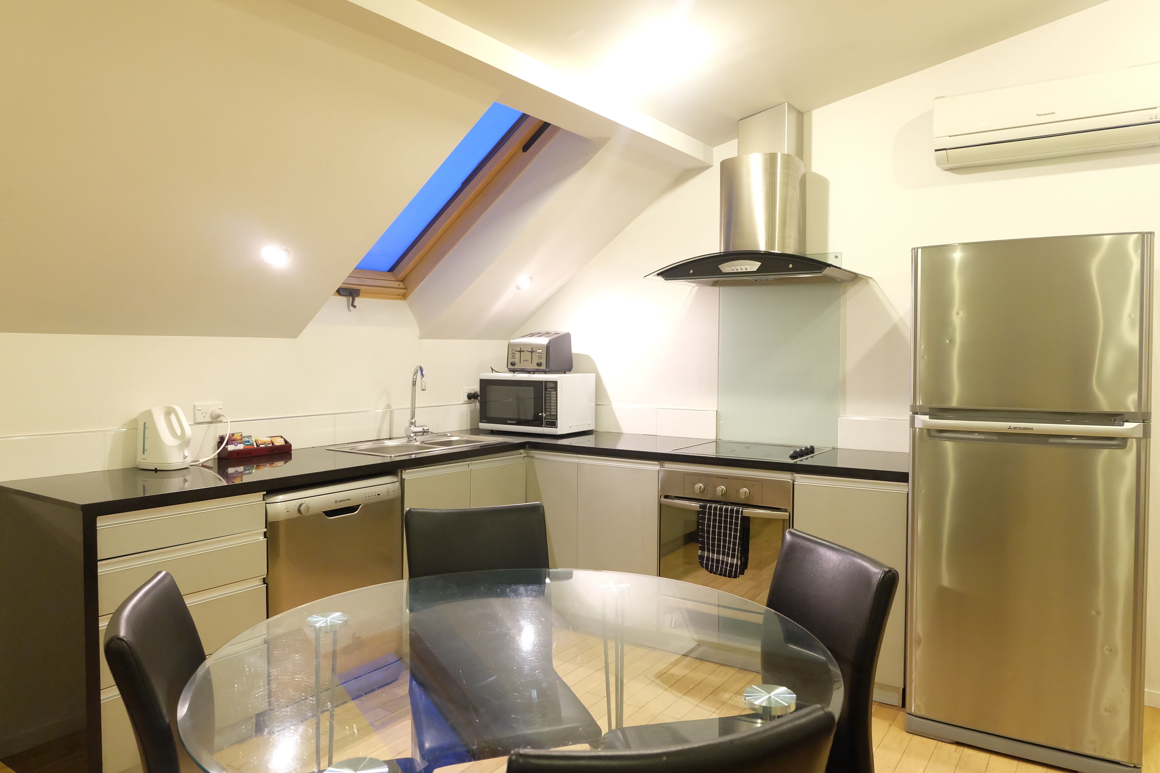 A modern kitchen with a skylight, stainless steel appliances, and a glass dining table.