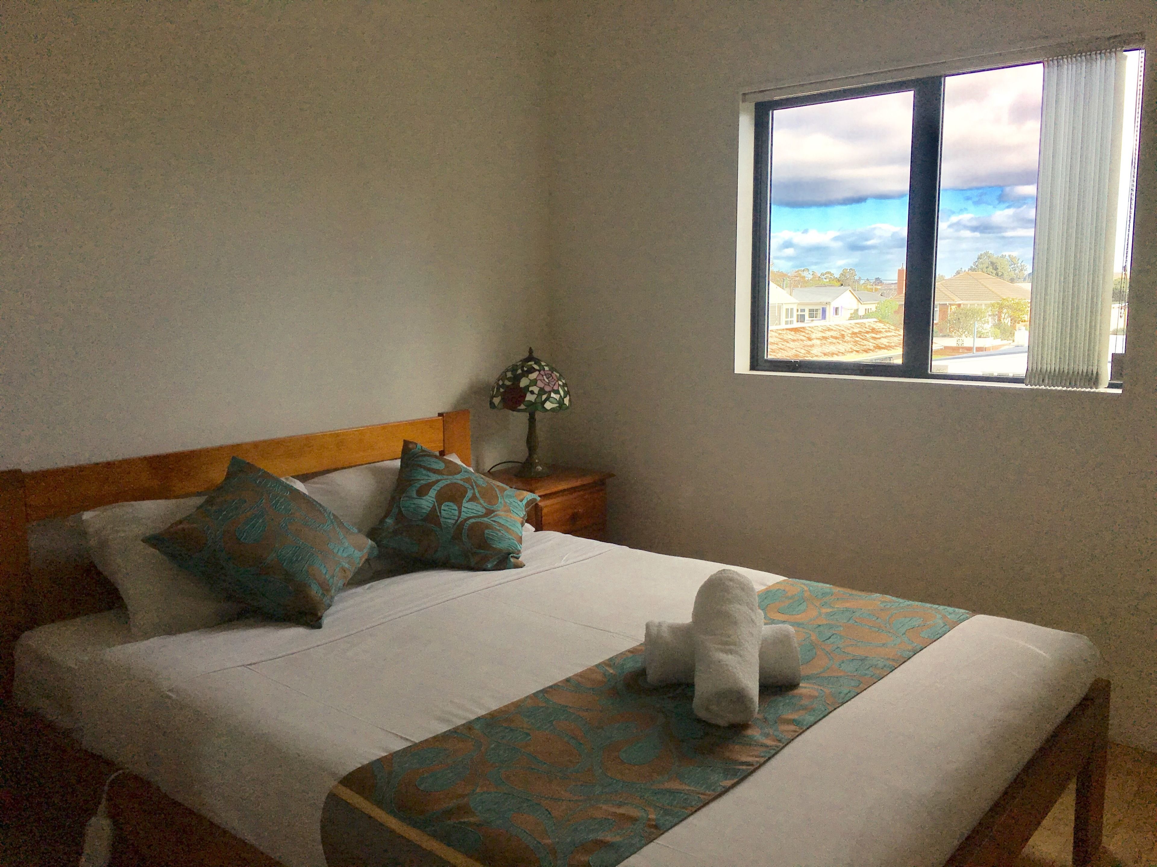 A bedroom with a bed, pillows, a bedside table with a lamp, and a window with a view.