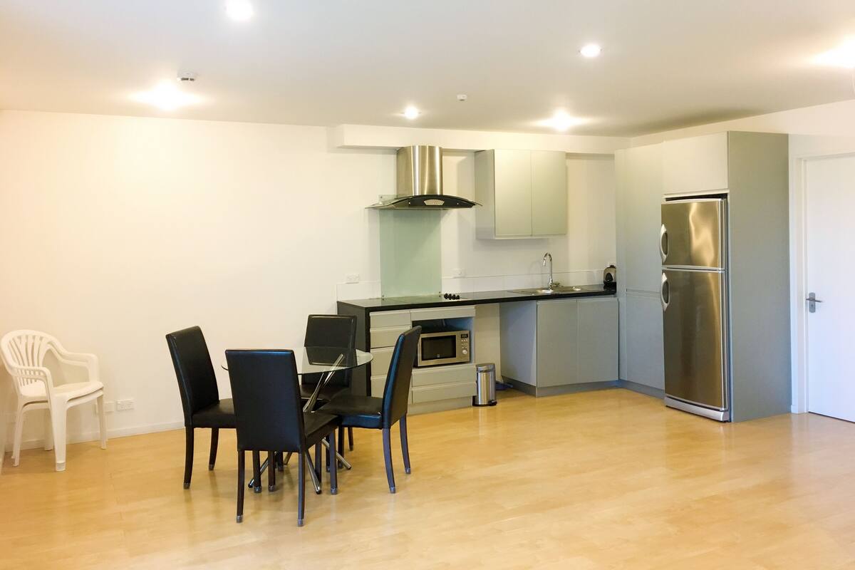 A compact kitchen with a dining area, white walls, and a stainless steel refrigerator.