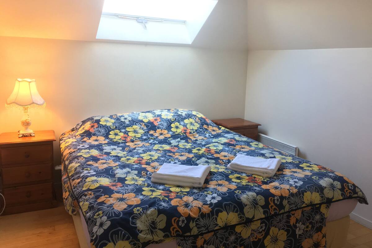 A bedroom with a bed, a nightstand, a lamp, and a window.