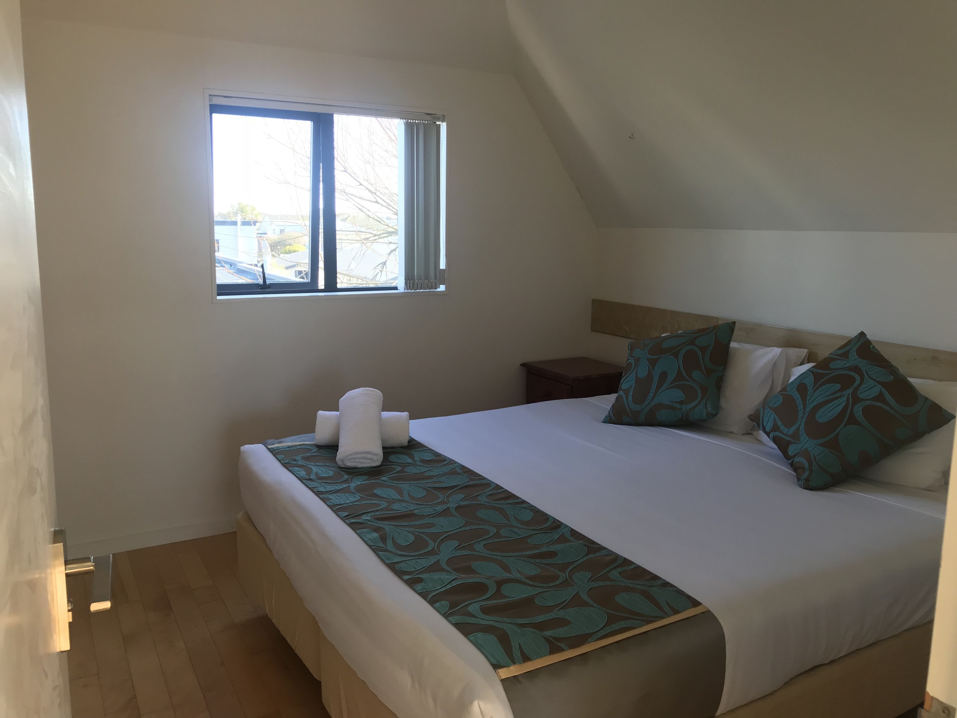 Un dormitorio con cama, ventana, mesita de noche y toalla.