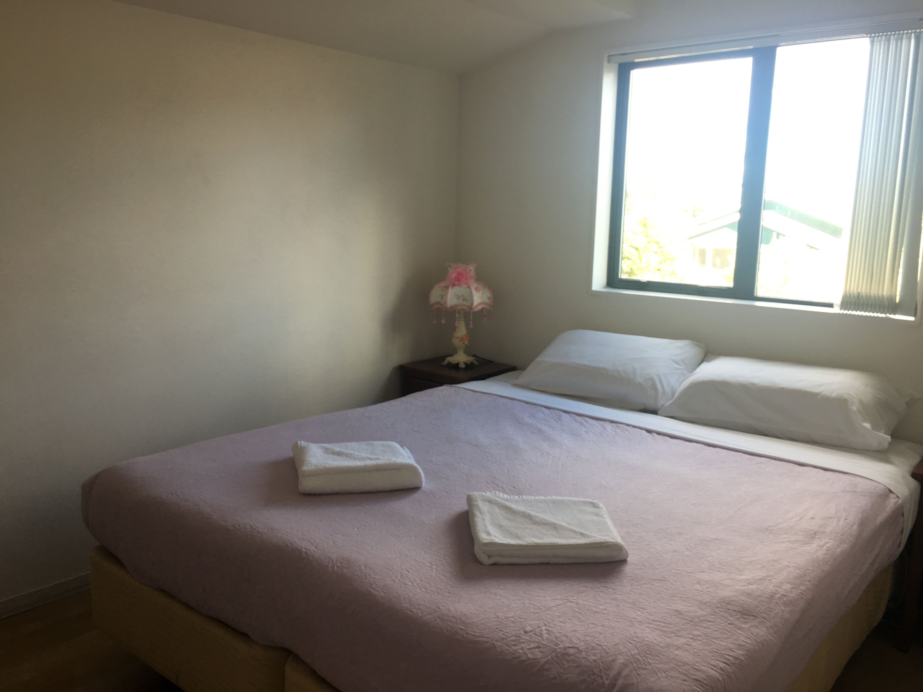 A bedroom with a bed, pillows, a nightstand, a lamp, and a window.