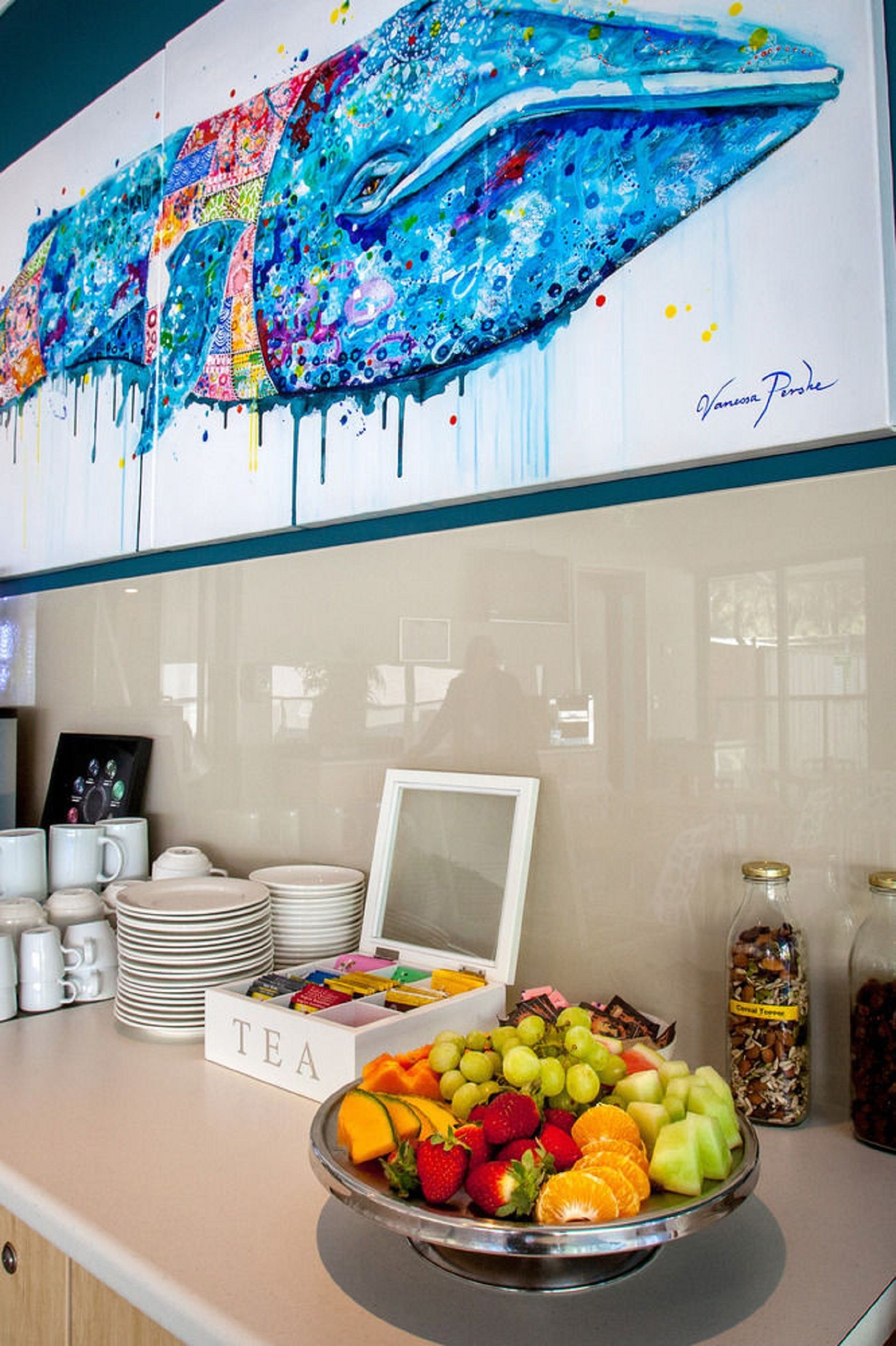 A buffet counter with a colorful whale painting, a tea sign, and a fruit bowl.
