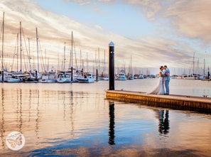 Una pareja abrazándose en un muelle, con un puerto deportivo al fondo.