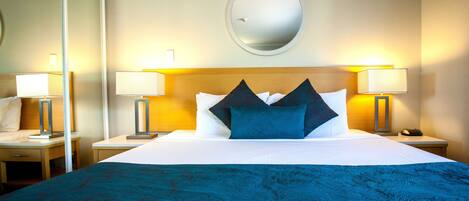 A hotel room with a large bed, two bedside lamps, a round mirror on the wall, and a nightstand with a phone.