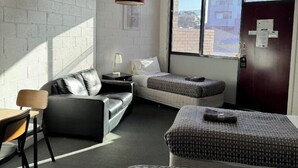 A modern hotel room with a sofa, a small table, a chair, a bed, and a large window offering a city view. - San Remo Hotel Motel (San Remo)