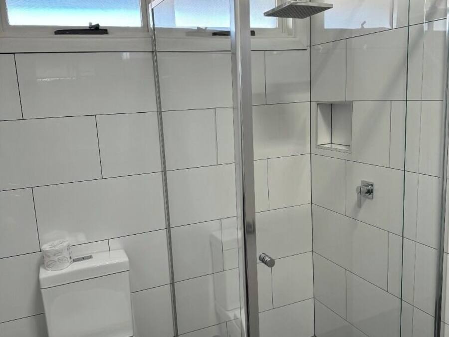 Un baño moderno con azulejos blancos, un inodoro, una ducha con puerta de vidrio y una ventana con vistas.
